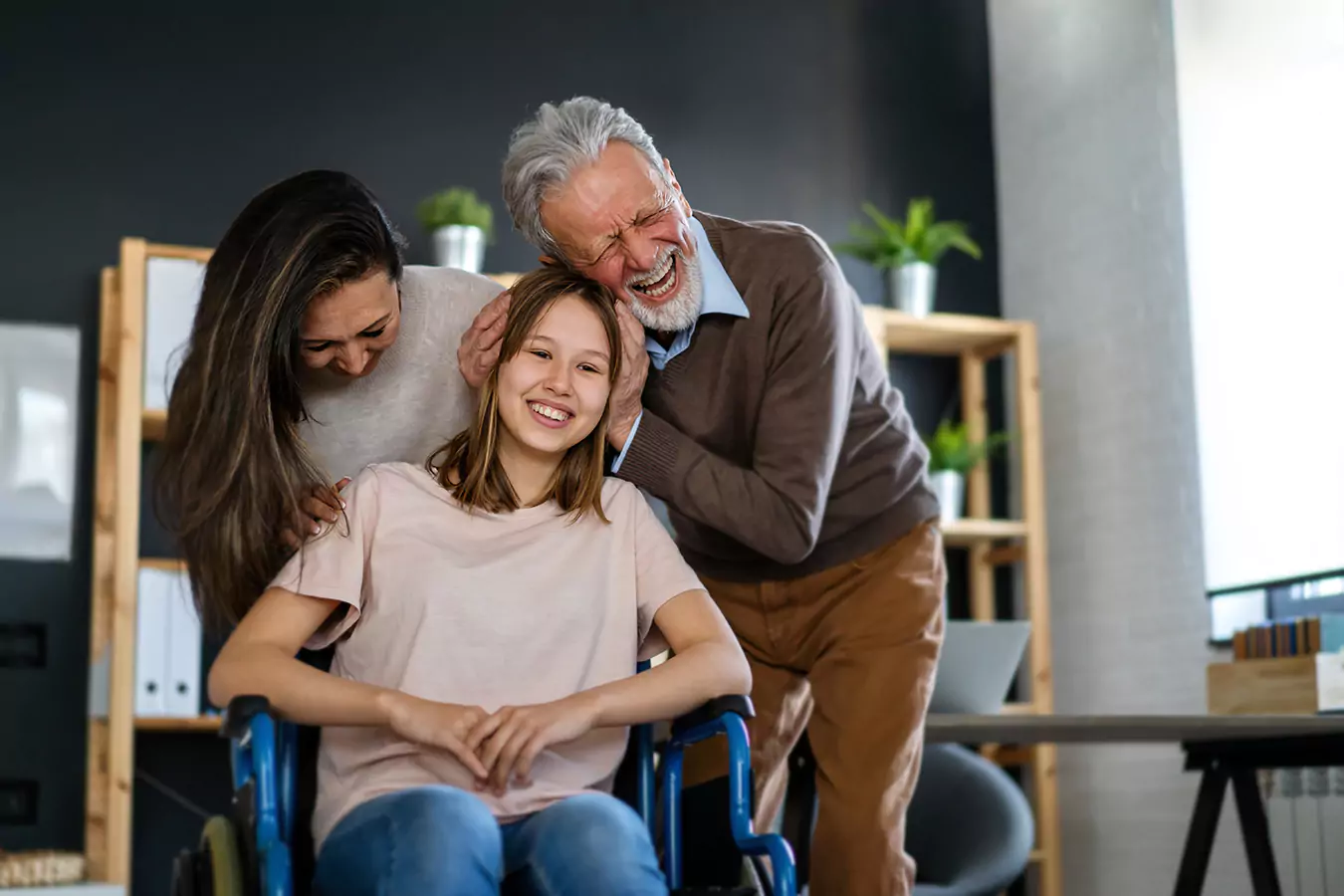 A disabled woman sitting in her wheelchair and her parents hugging her